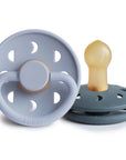 Two Frigg Moon Rubber baby pacifiers, one Powder Blue and one Slate, on a white background.
