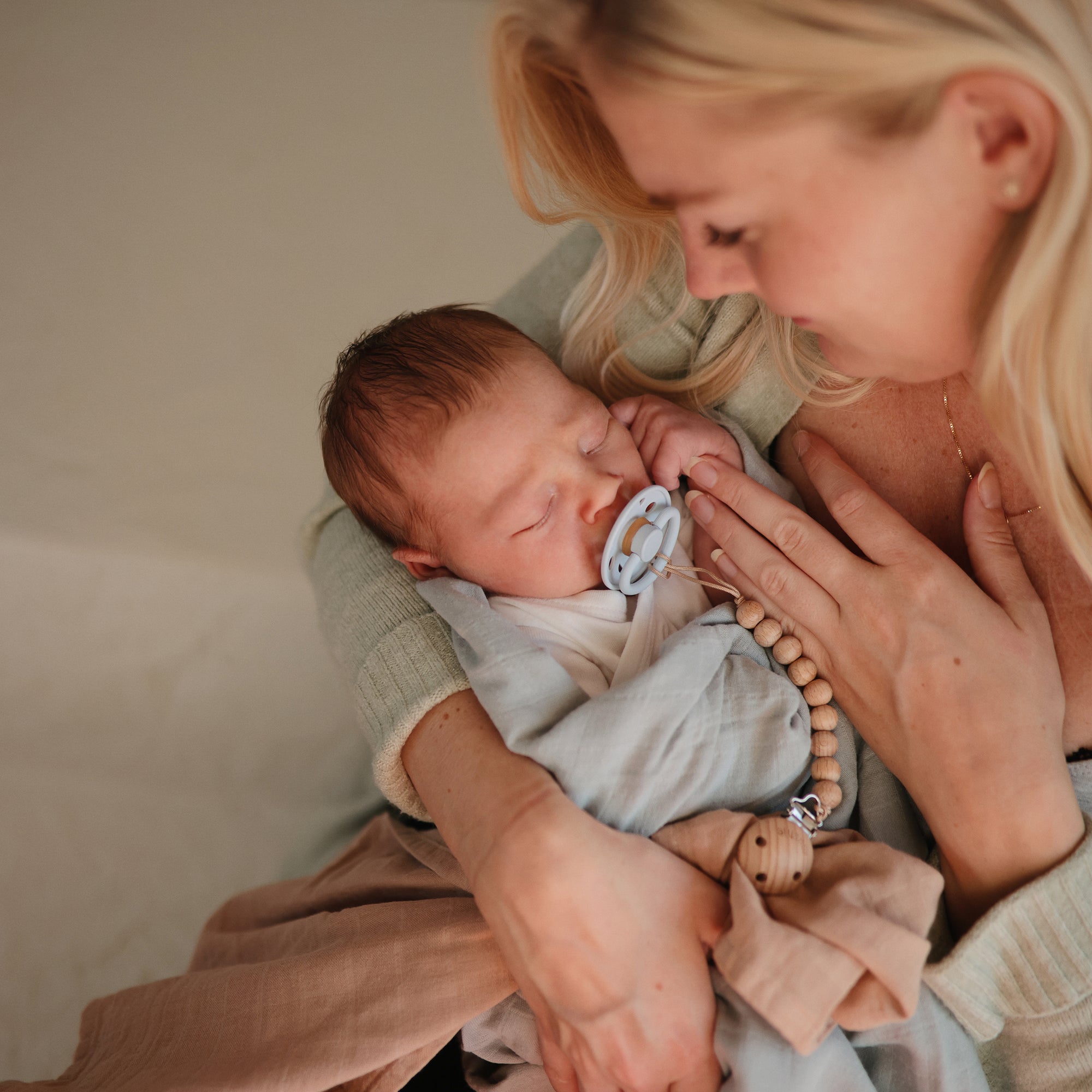 Lifestyle image of a mom holding a newborn baby with a Frigg Moon rubber pacifier in Powder Blue.