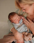 Lifestyle image of a mom holding a newborn baby with a Frigg Moon rubber pacifier in Powder Blue.