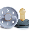 Two Frigg Moon Rubber baby pacifiers, one Powder Blue and one Slate, on a white background.