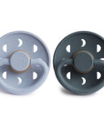 Two Frigg Moon Rubber baby pacifiers, one Powder Blue and one Slate, on a white background.