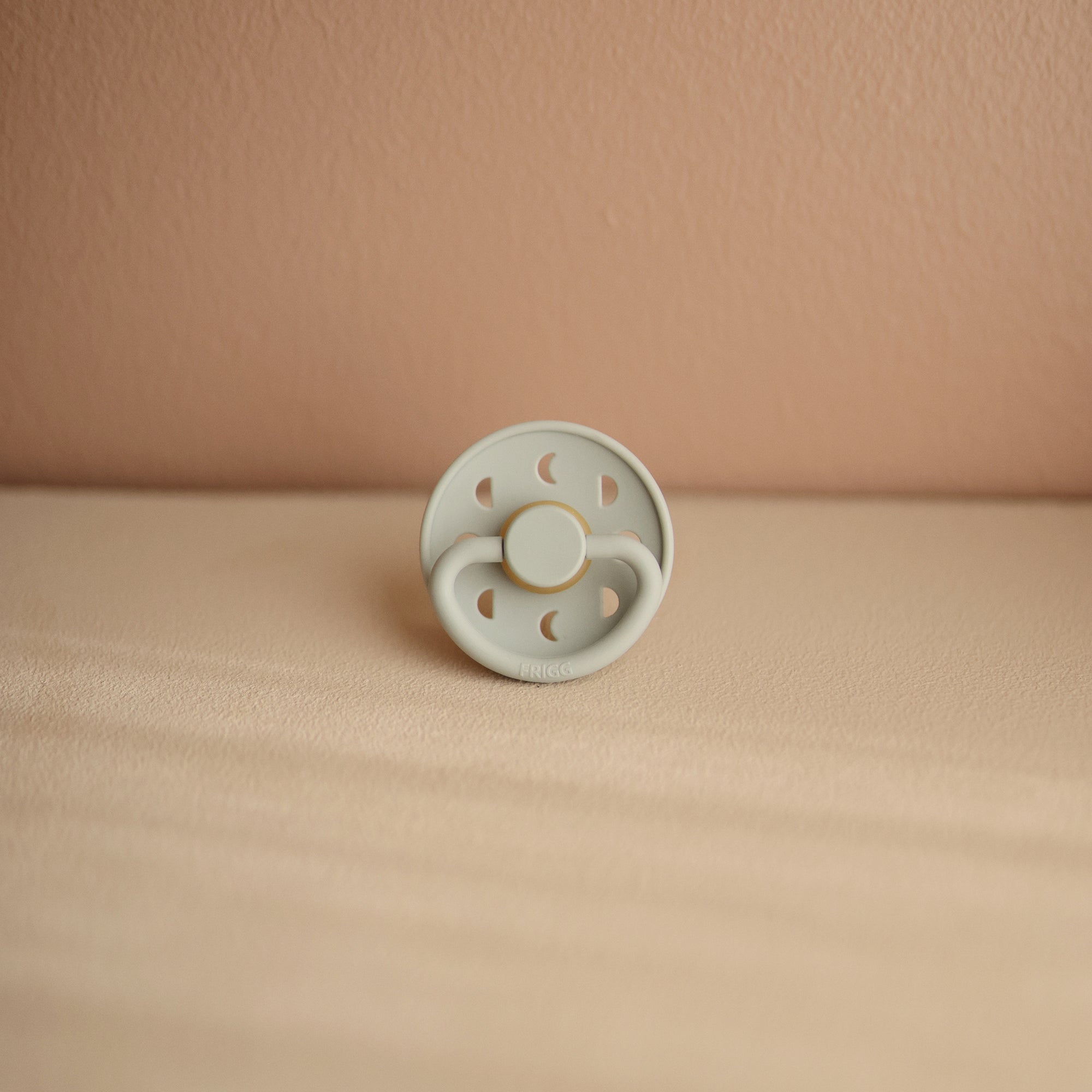 Lifestyle image of a Frigg Moon Rubber pacifier with a decorative moon design on the pacifier shield in Sage. 