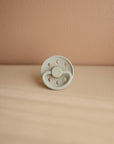 Lifestyle image of a Frigg Moon Rubber pacifier with a decorative moon design on the pacifier shield in Sage. 