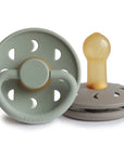 Two Frigg Moon Rubber baby pacifiers, one Sage and one Portobello, on a white background.