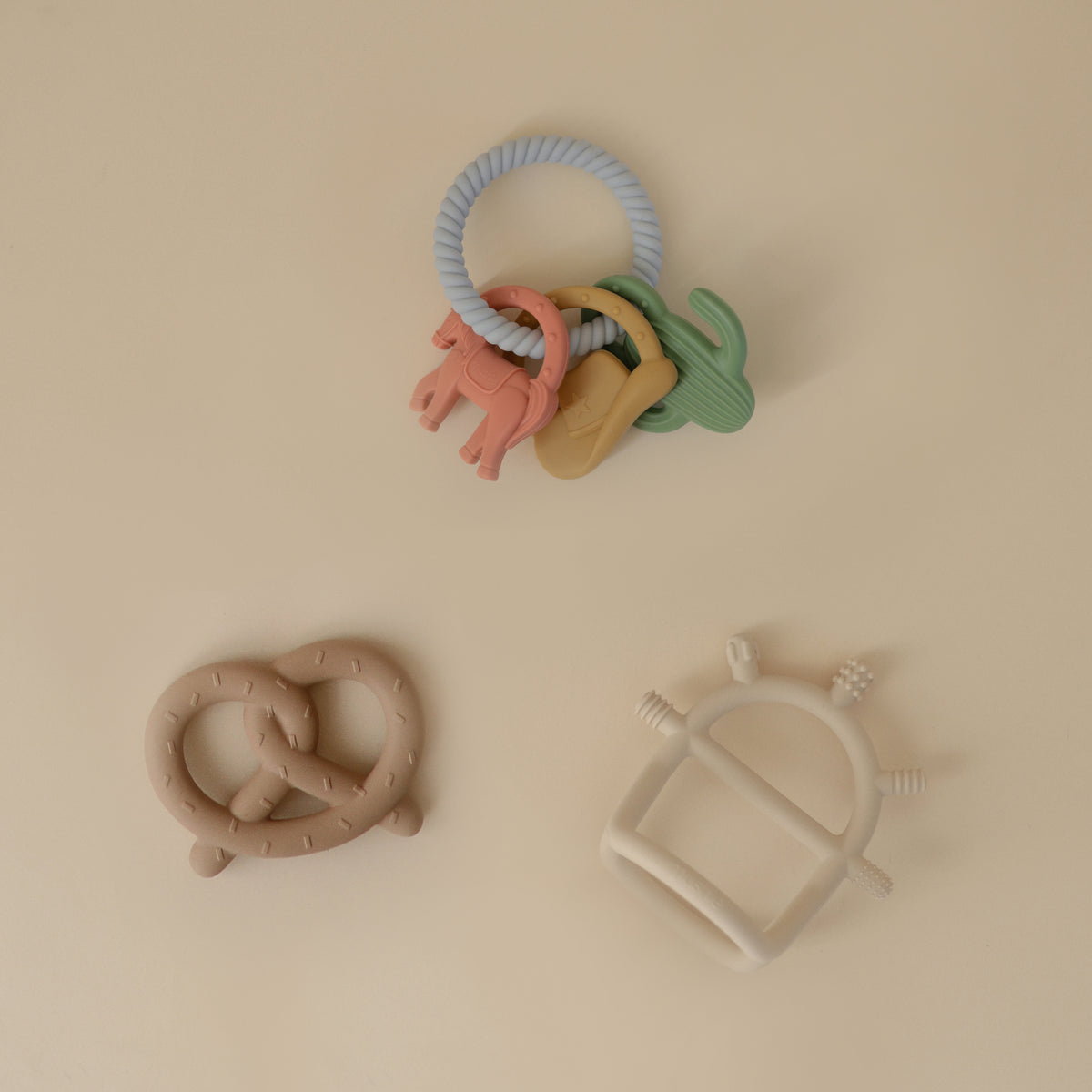 Mushie Teething Gift Set: 3 pastel silicone teethers displayed on a beige background.