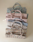Lifestyle image of a stack of mushie Diaper Caddies in various colors and patterns on a beige background.