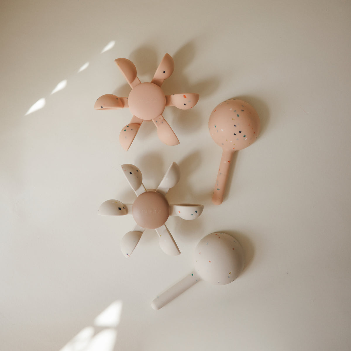 Two flower-shaped silicone teethers and two mushie Water Wheel Bath Toys on a light surface.