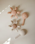 Two flower-shaped silicone teethers and two mushie Water Wheel Bath Toys on a light surface.