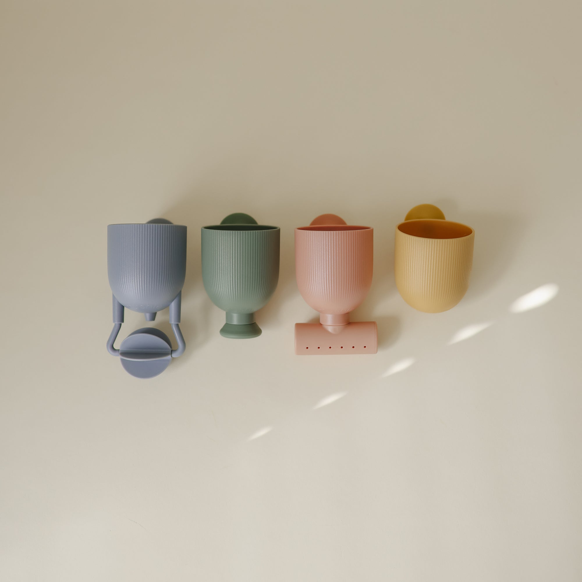 Four mushie Pour and Play Bath Set cups with handles, lined up on a cream background.