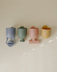 Four mushie Pour and Play Bath Set cups with handles, lined up on a cream background.
