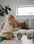 Child playing with mushie sensory toys on a table in a living room