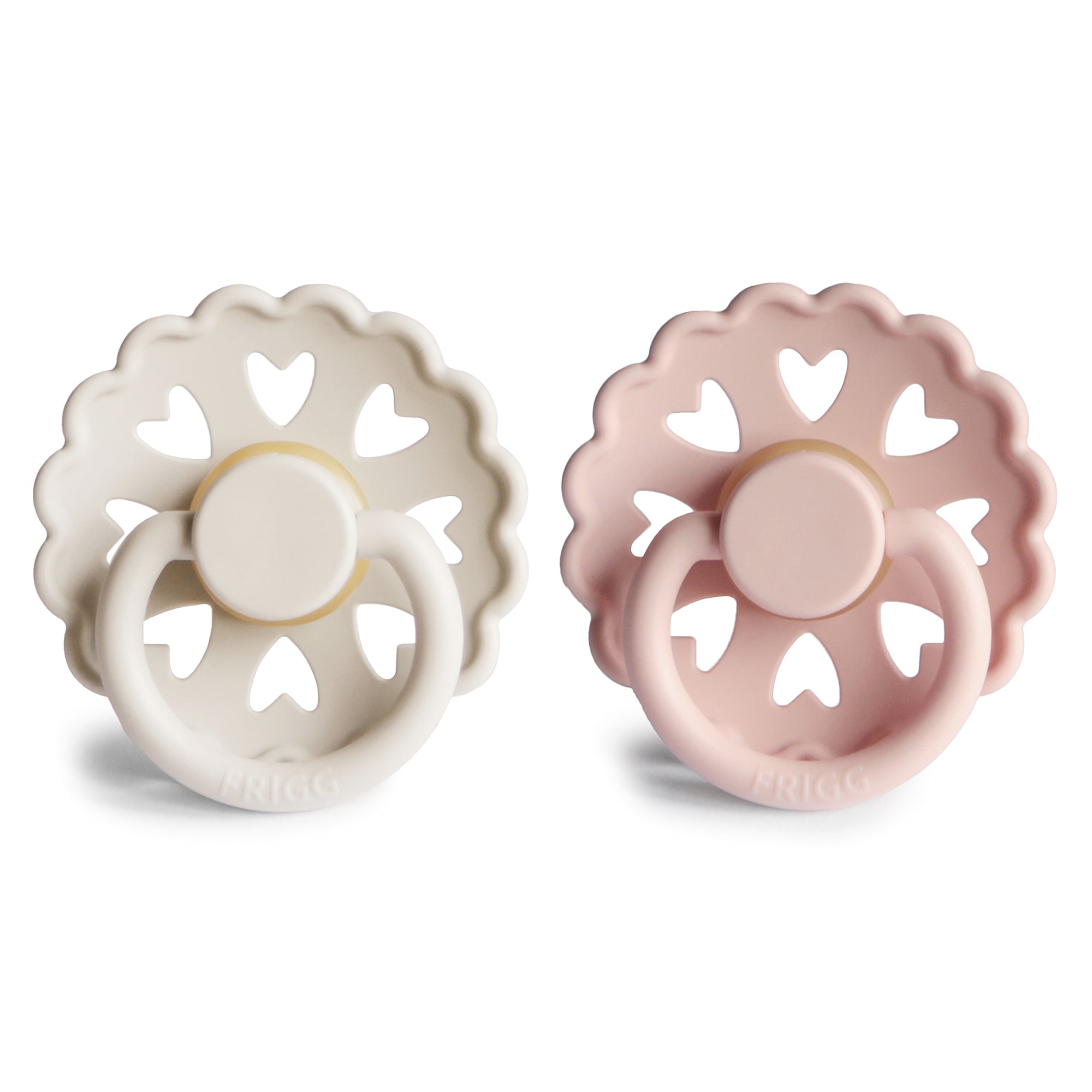 Two decorative Frigg Andersen pacifiers, one Cream and one Blush, on a white background
