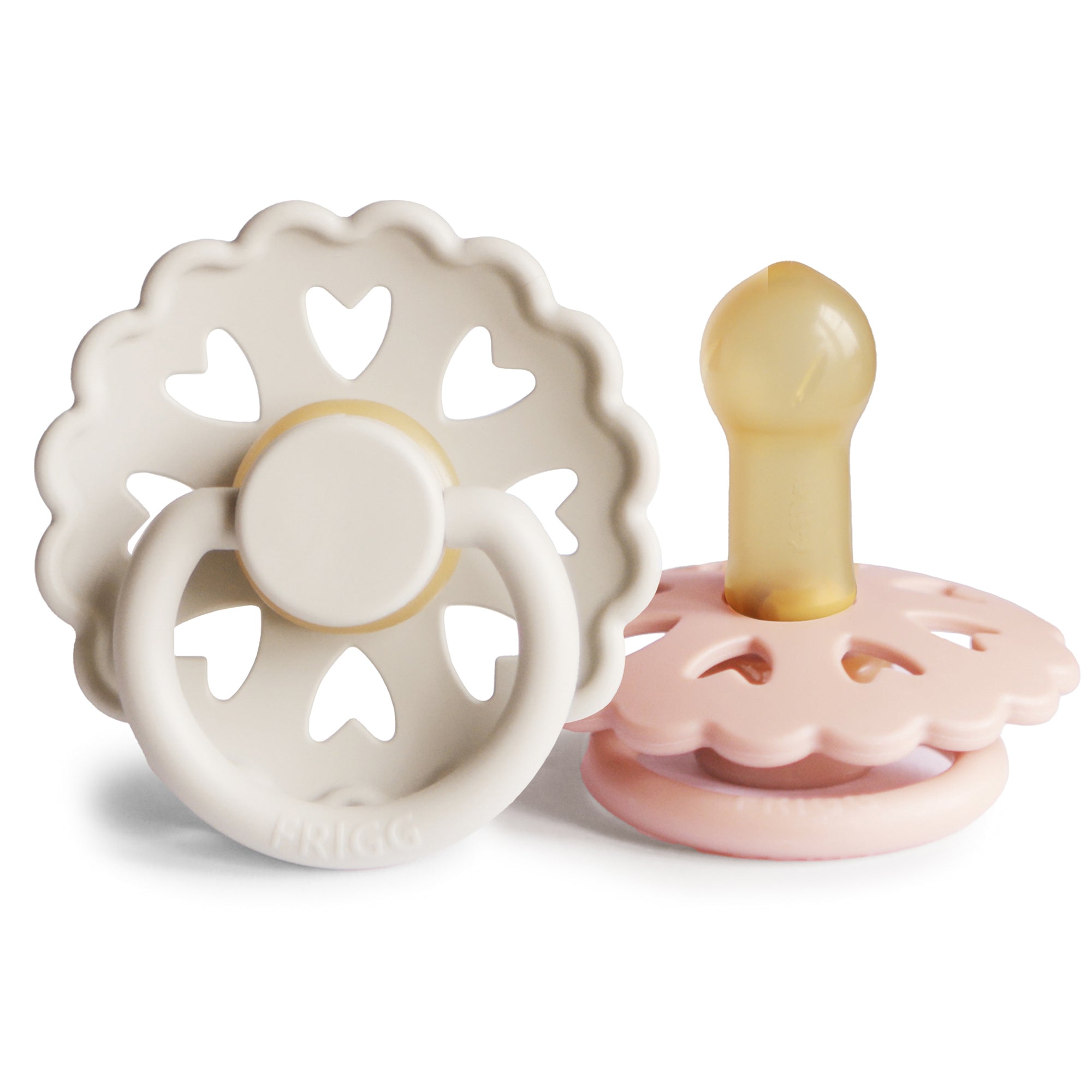 Two baby Frigg Andersen Rubber pacifiers, one Cream with heart designs and the other Blush on a white background.