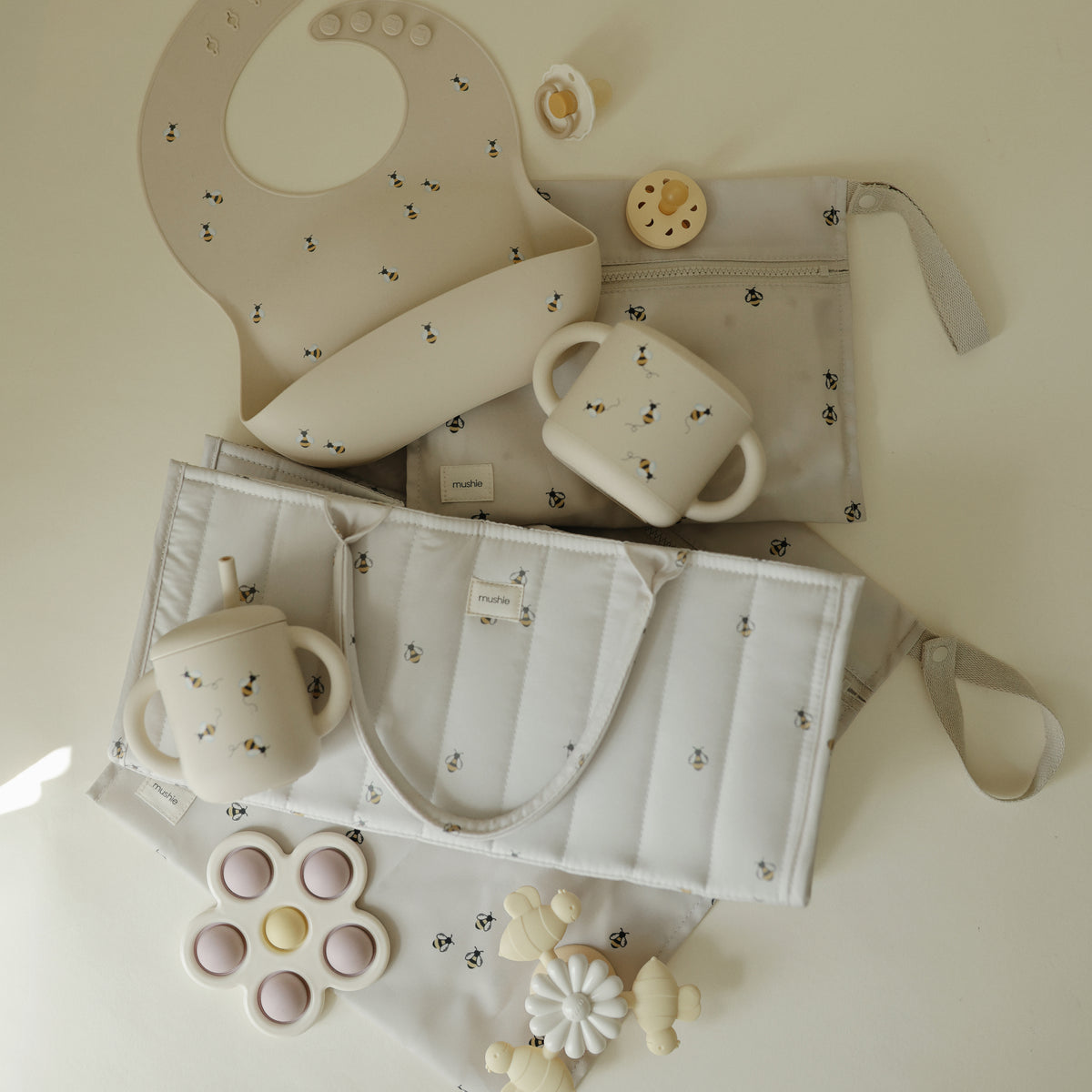 Mushie Diaper Caddy, bib, toys &amp; neutral feeding items displayed on a light surface.