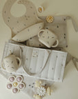 Mushie Diaper Caddy, bib, toys & neutral feeding items displayed on a light surface.