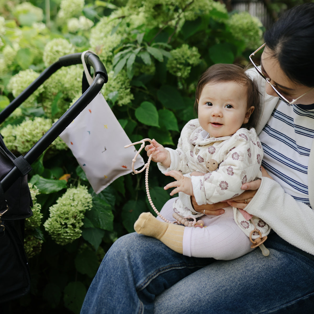 A parent holds a baby near a stroller with a mushie Water Resistant Wet Bag on the handle.