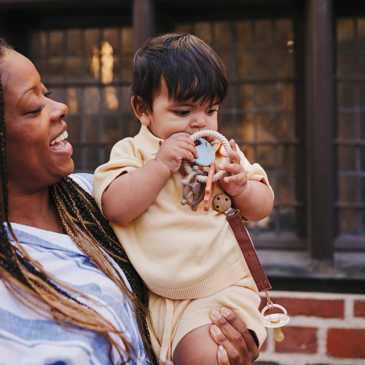 A woman holds a baby chewing on a textured, food-grade silicone mushie Teething Ring.