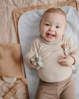 Smiling baby holding a toy while lying on a Mushie Changing Pad Liner.