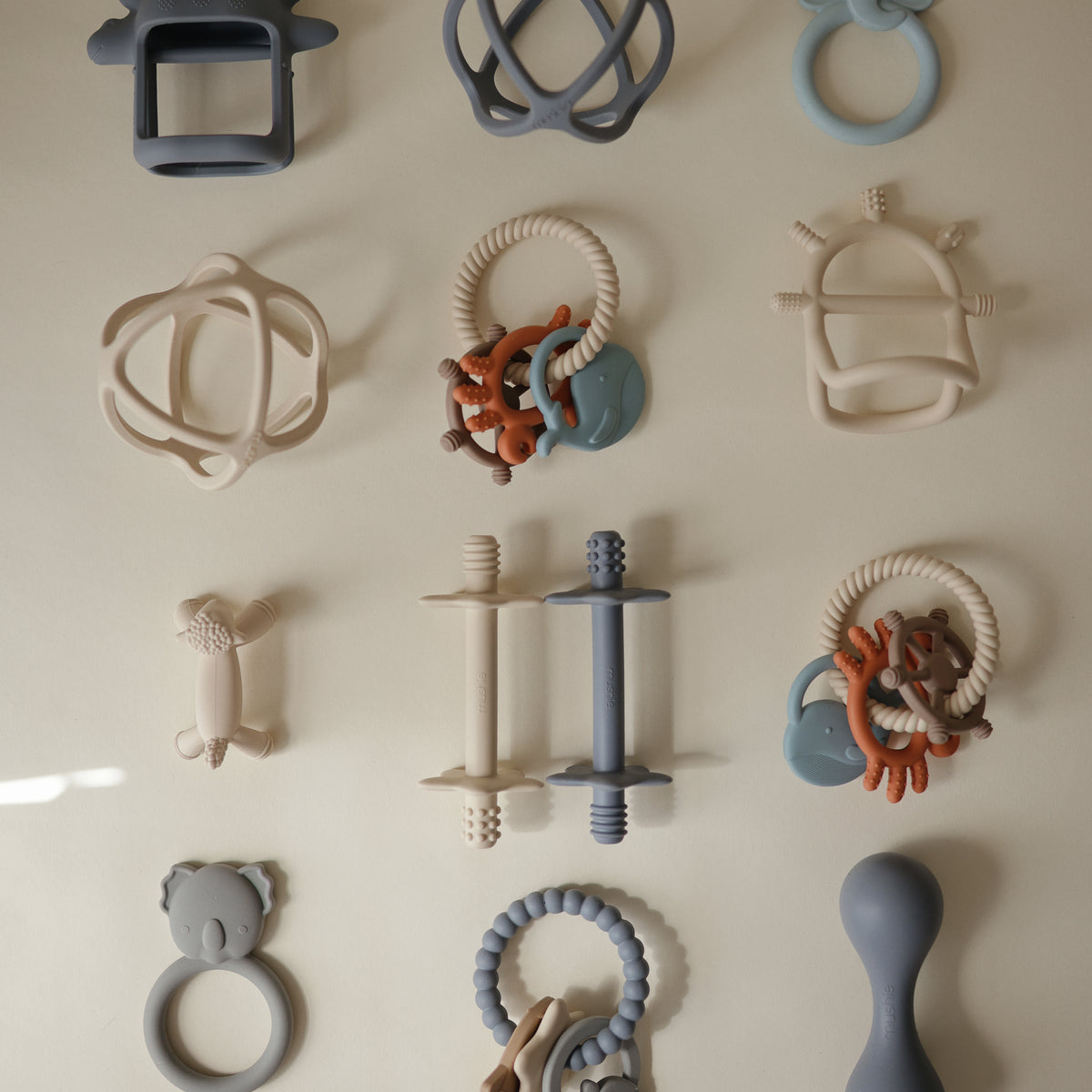 A grid of twelve mushie Teething Rings in various shapes and muted colors.