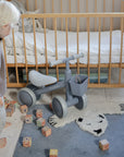 A toddler stands next to a mushie Mini Toddler Bike with a front basket and wooden letter blocks.