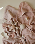 Soft pink baby towel with pacifier, rattle, and mushie Water Wheel Bath Toy on top.