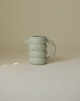 Light green, ribbed Mushie Silicone Watering Can for water play with colorful speckles.