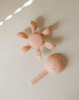 Two mushie Water Wheel Bath Toys, pink round and flower, speckled, on a beige surface.