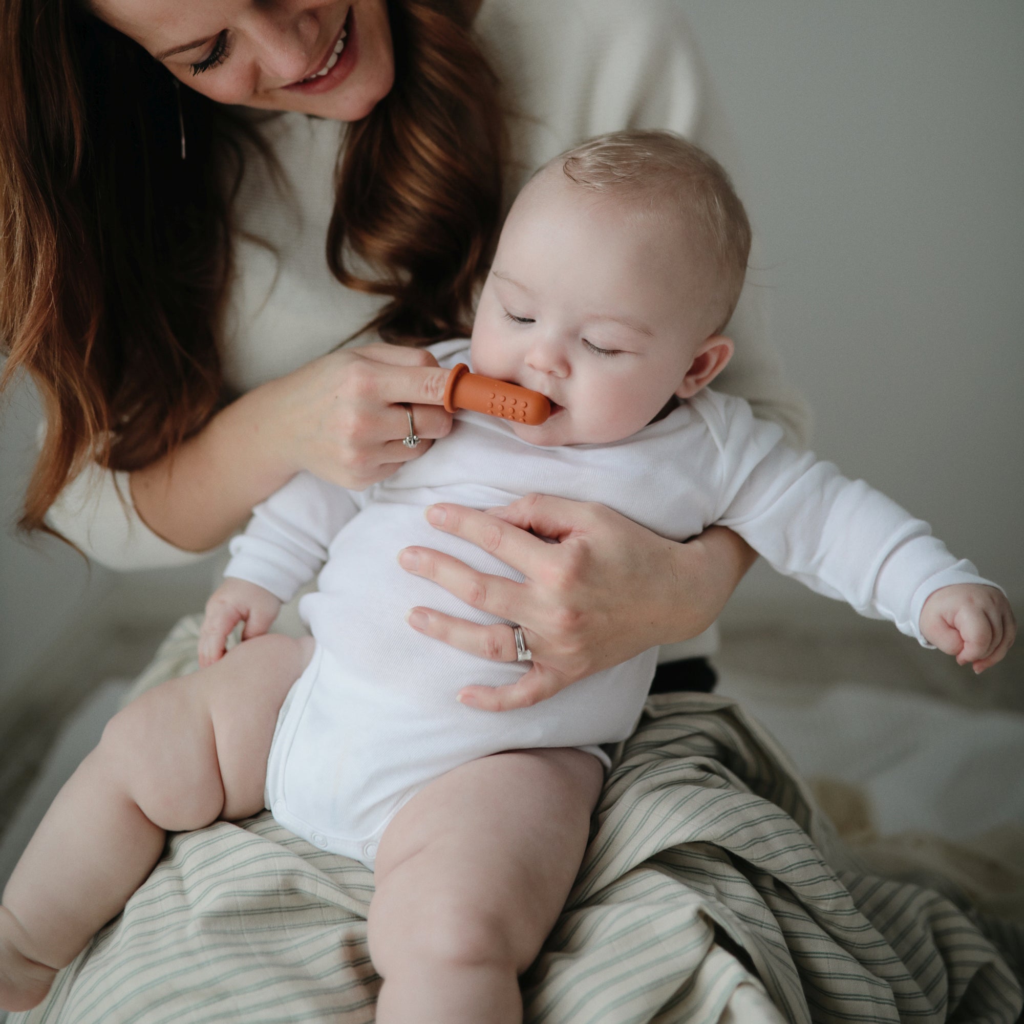 A smiling woman swaddles her baby in a mushie Organic Cotton Muslin Swaddle Blanket.