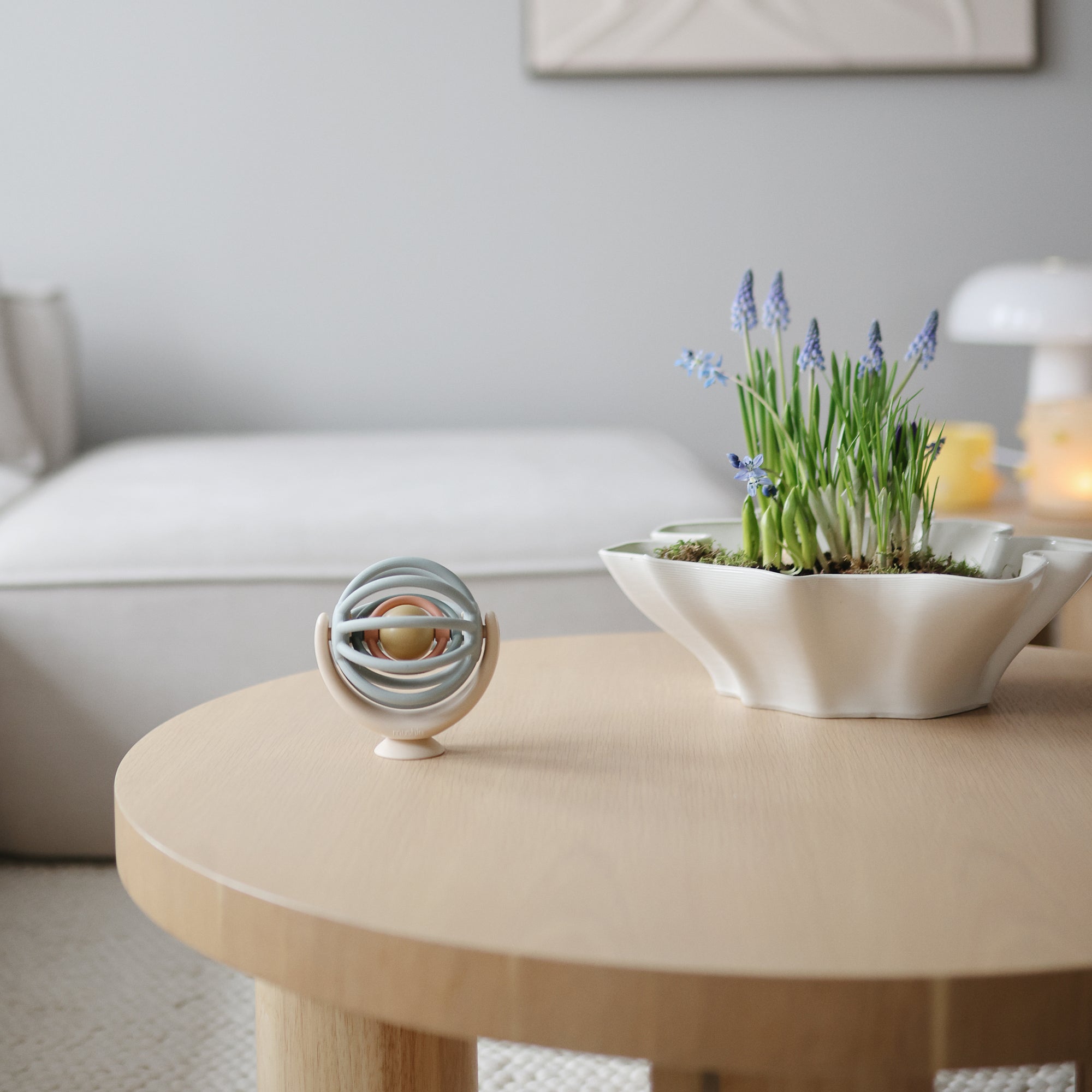 Round wooden coffee table with decorative items including a bowl of plants and a mushie suction spinner ball toy in a living room setting.