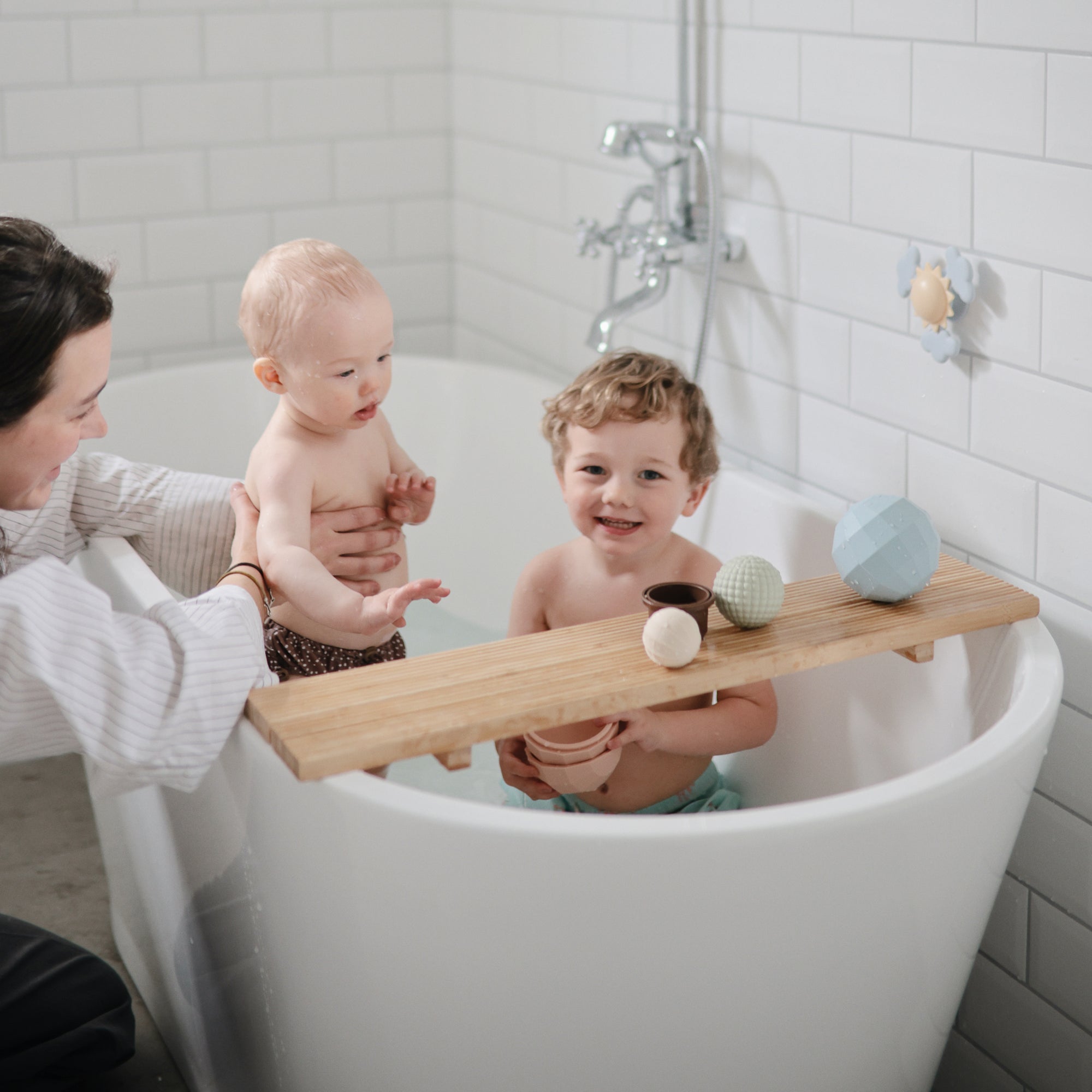 Two small children play with mushie's Nesting Spheres Sensory Toy on a wooden bath tray.