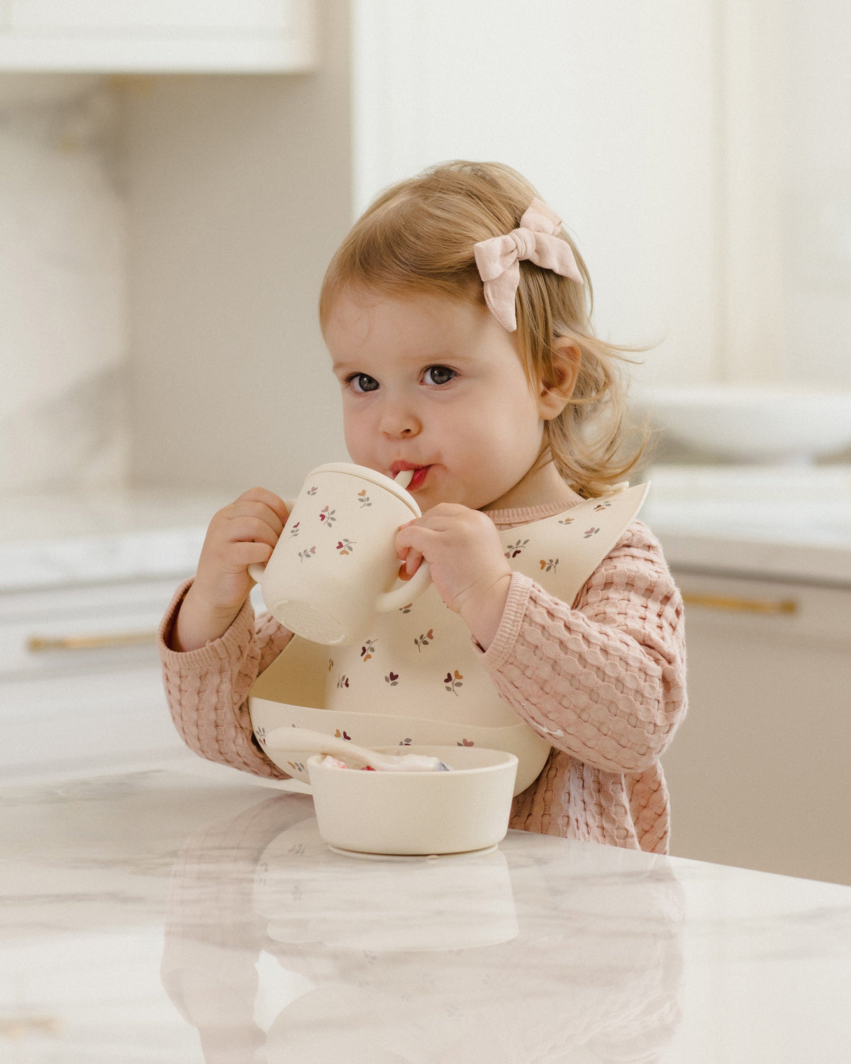 Toddler drinks from Feeding Kit Heart Ditsy by Rylee + Cru, wearing bib at kitchen counter.
