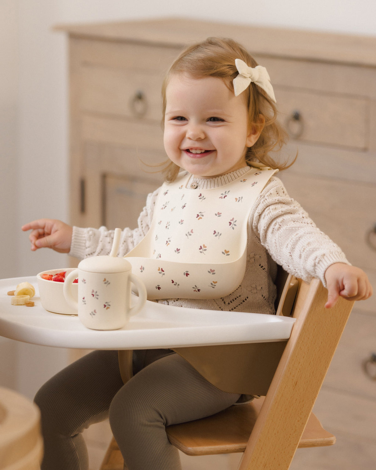 Smiling toddler in a high chair with Rylee + Cru Feeding Kit Heart Ditsy, bib, and suction bowl.