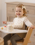 Smiling toddler in a high chair with Rylee + Cru Feeding Kit Heart Ditsy, bib, and suction bowl.