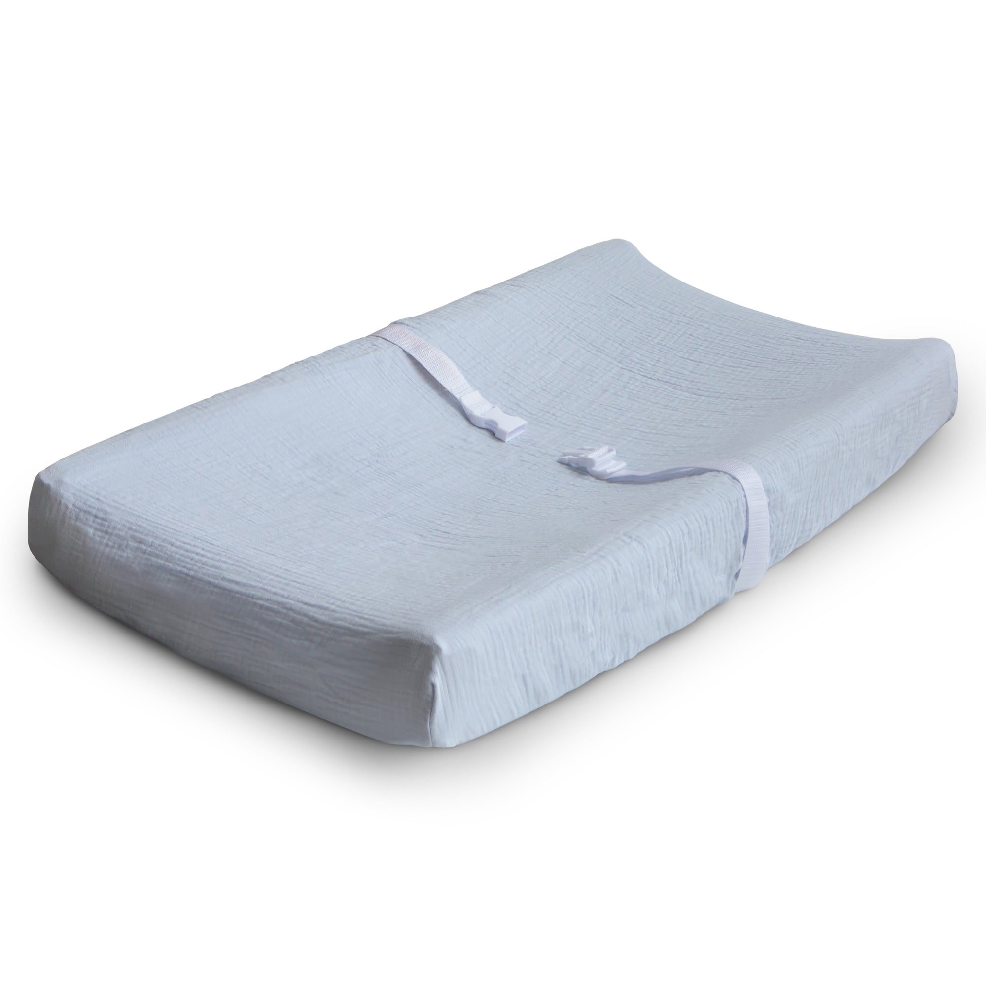 The mushie Extra Soft Muslin Changing Pad Cover is shown on a contoured white pad with safety straps, designed for changing babies, displayed on a plain white background.