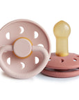 Two FRIGG Moon Natural Rubber Pacifiers, pink, one upright and one lying down.