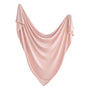 The mushie Stretchy Swaddle in soft light pink is draped in a wide, gentle curve with flowing folds and a triangular shape against a white background.