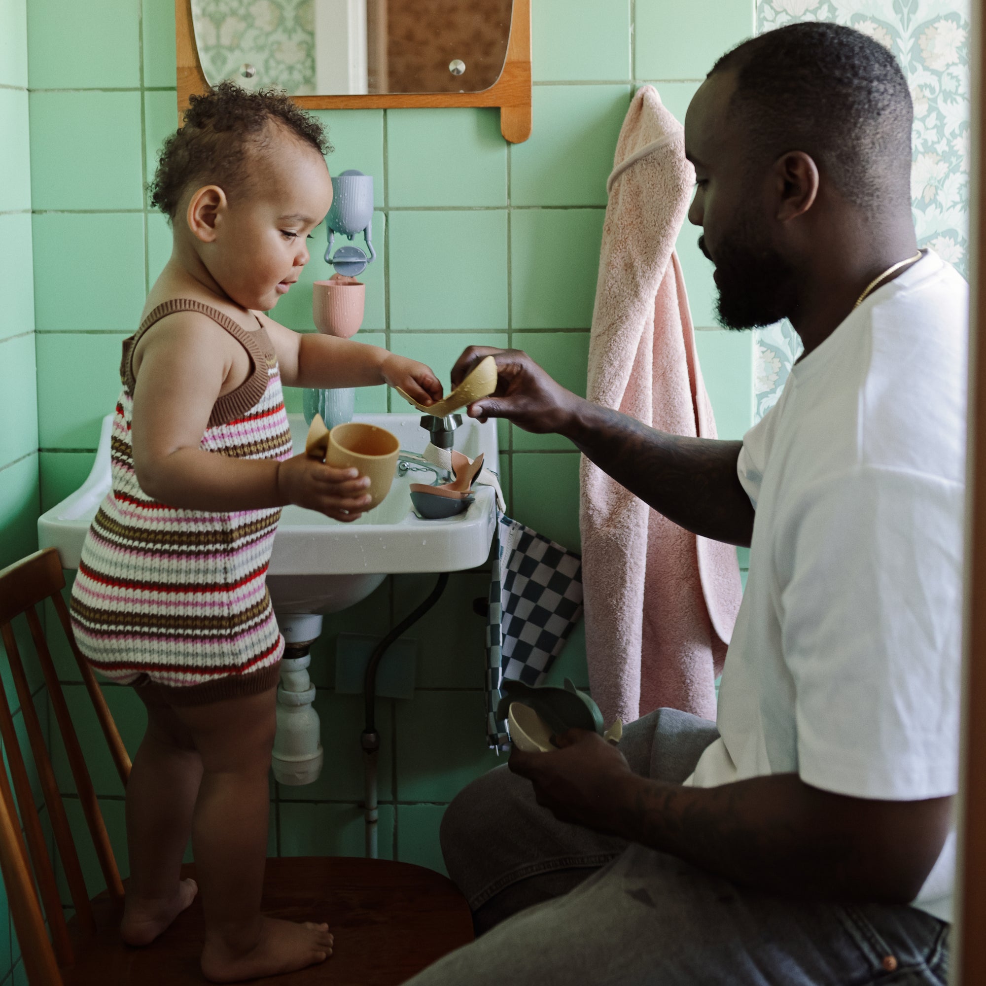 A man and toddler play with Mushie Whale Bath Stackers by the bathroom sink.
