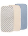 Three Mushie Changing Pad Liners—checkered, beige, and blue—overlapping each other.