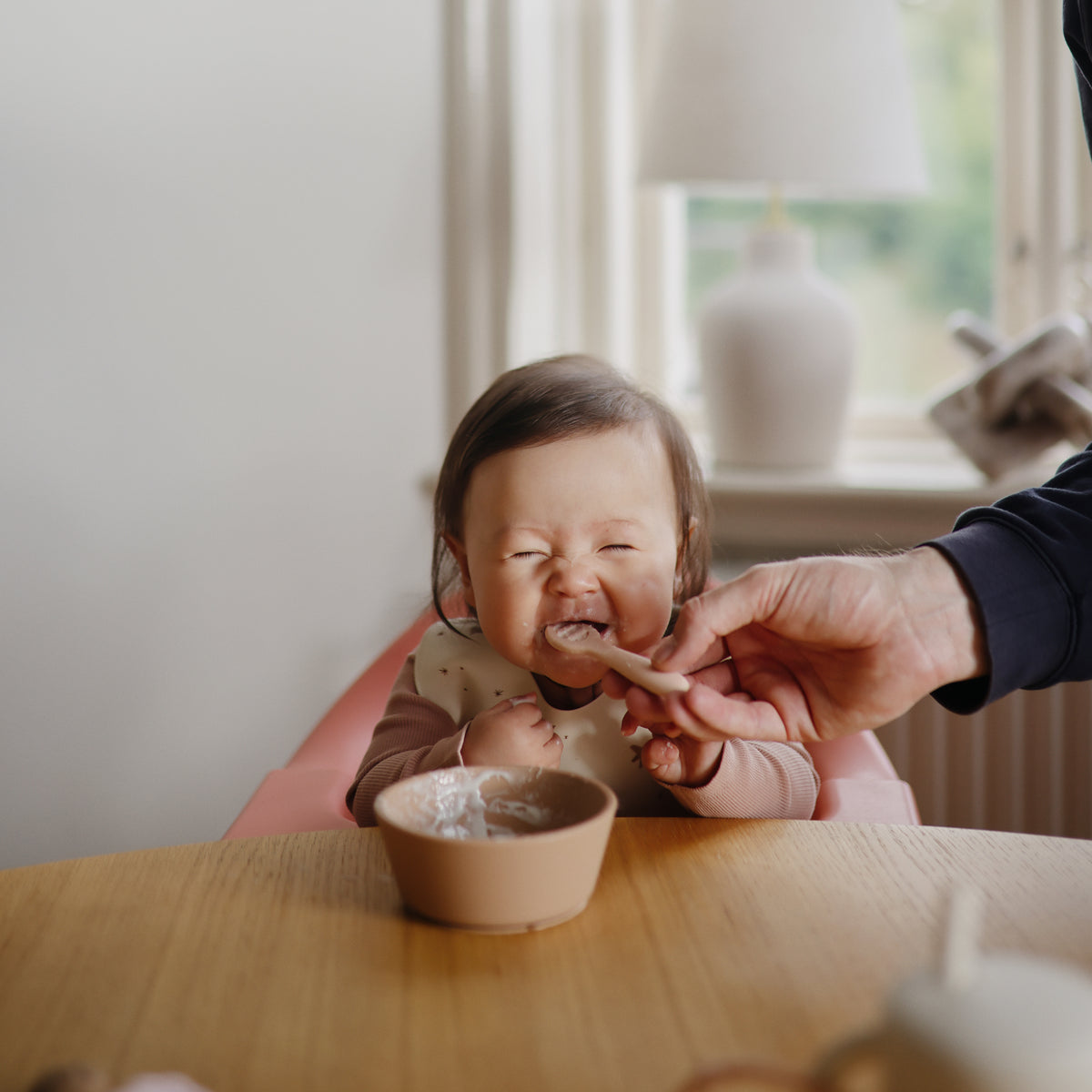 Mushie First Feeding Baby Spoons make mealtime joyful, with baby eating at their table and bowl.