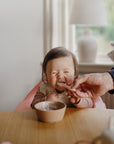 Mushie First Feeding Baby Spoons make mealtime joyful, with baby eating at their table and bowl.