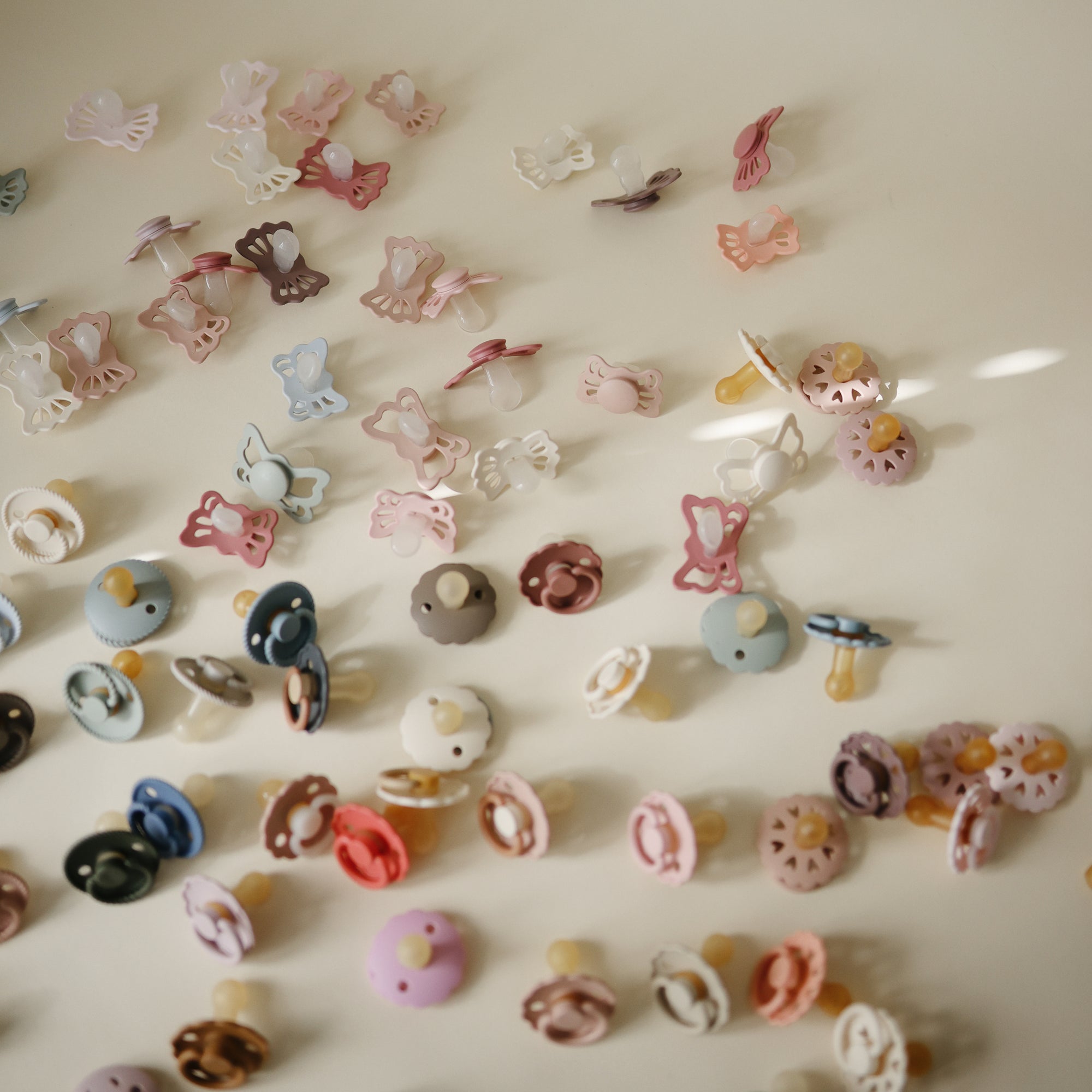 FRIGG Daisy Natural Rubber Pacifier 2-Pack pacifiers scattered on a light surface.