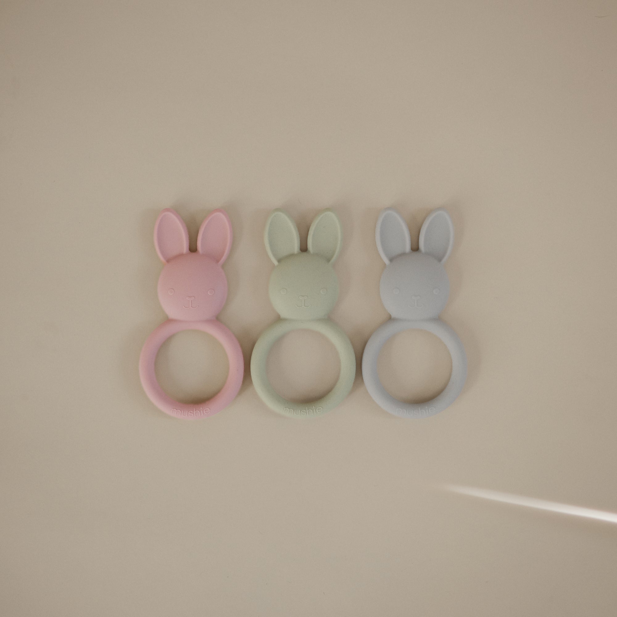 Three mushie Bunny Teethers in pink, green, and blue silicone on a light background.
