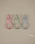 Three mushie Bunny Teethers in pink, green, and blue silicone on a light background.