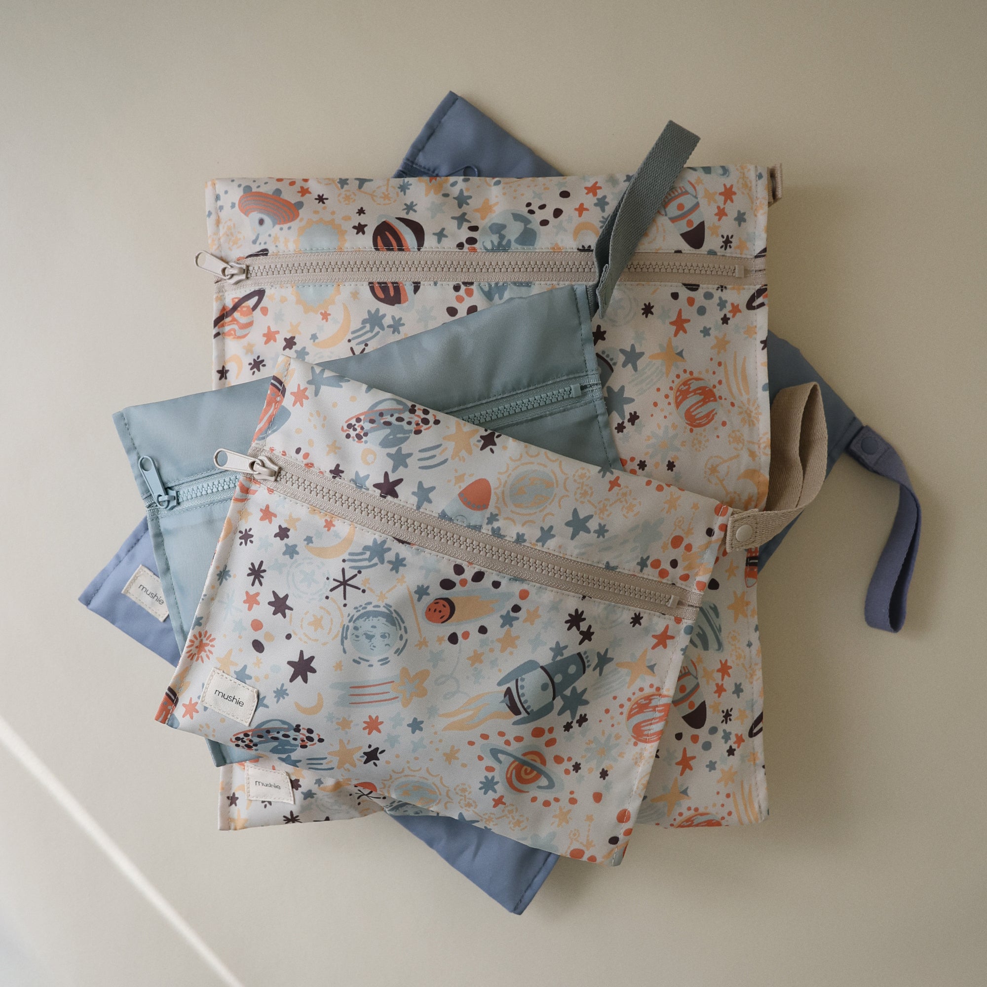 Four mushie Water Resistant Wet Bags with space designs are displayed on blue backgrounds.