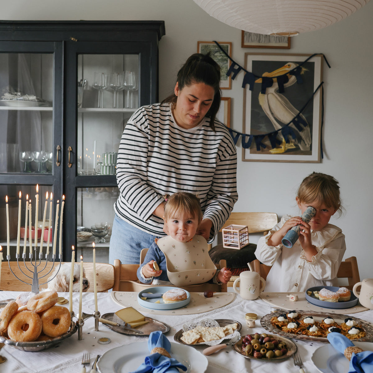 Mom with two kids at a festive table; one wears mushie’s colorful Silicone Baby Bib.