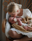 A young girl kisses a swaddled baby holding a FRIGG Daisy Natural Rubber Pacifier.