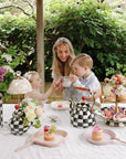 A woman and two kids use mushie's Dinnerware Fork and Spoon Set at a lovely outdoor tea table.