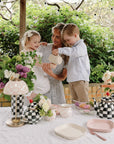 A woman and two kids use mushie's Dinnerware Fork and Spoon Set at a floral outdoor tea party.
