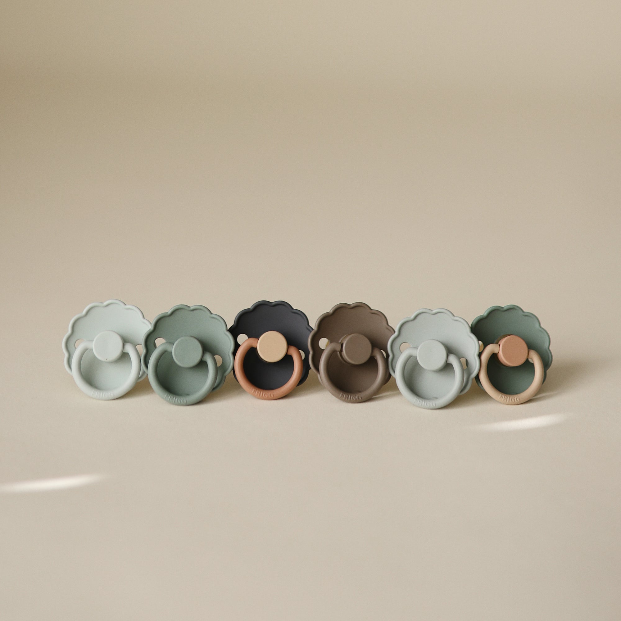 Six FRIGG Daisy Natural Rubber Pacifiers (3 packs of 2) lined up on a beige surface.