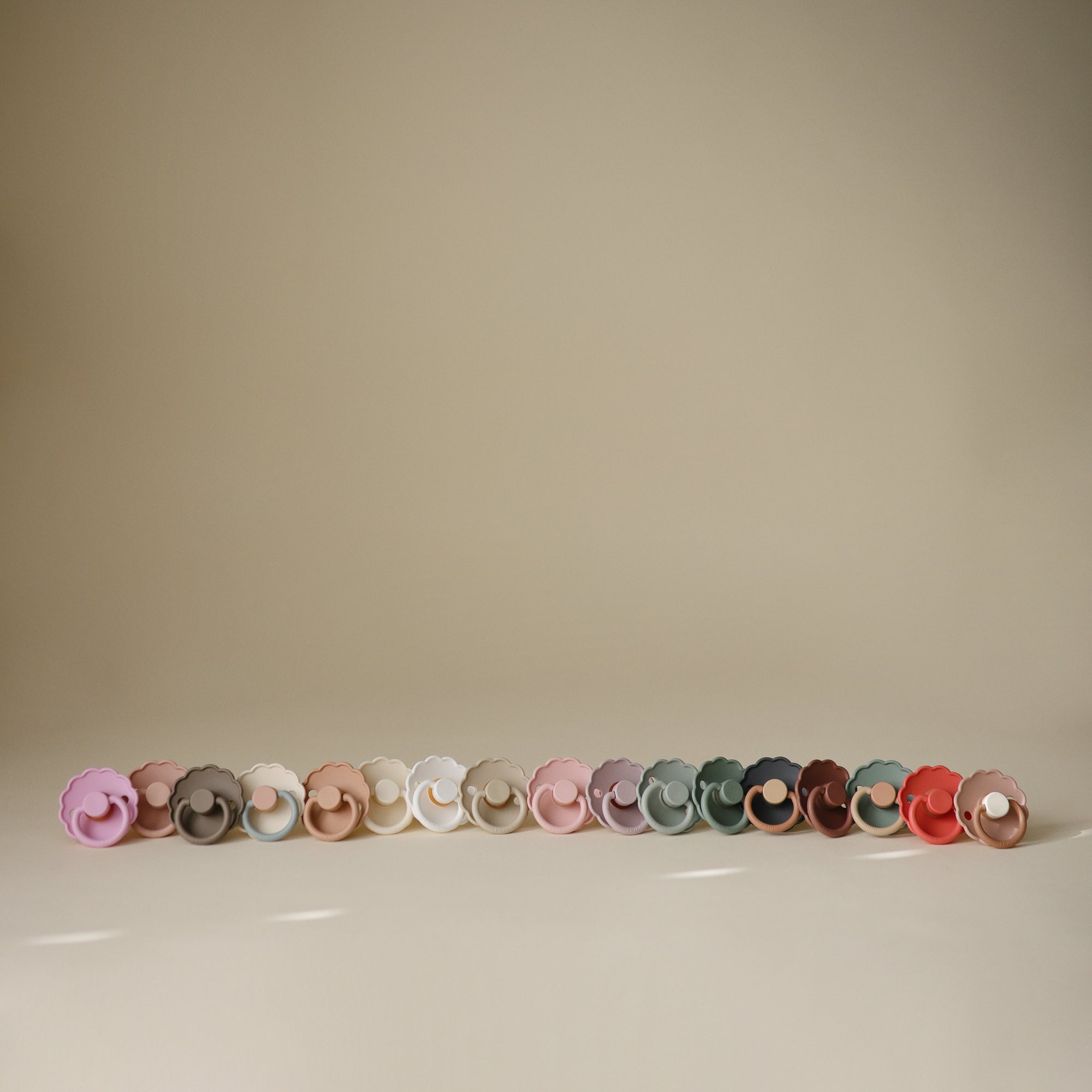 FRIGG Daisy Natural Rubber Pacifier 2-Pack in assorted colors on a light beige background.